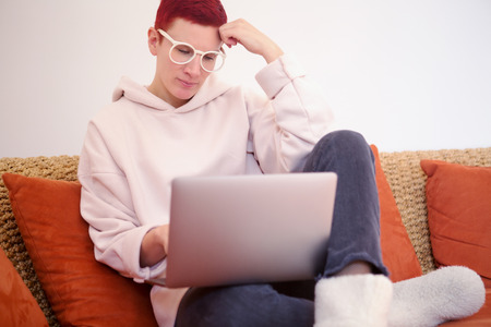 red-haired woman sitting on couch with her laptopの写真素材