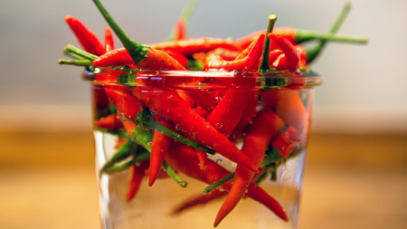 close up of red chilis in a jar with water on wooden tableの写真素材