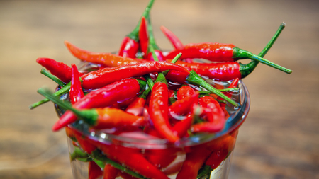 close up of red chilis in a jar with water on wooden tableの写真素材