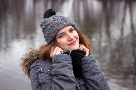 Beautiful young woman standing by the water in the coldの写真素材
