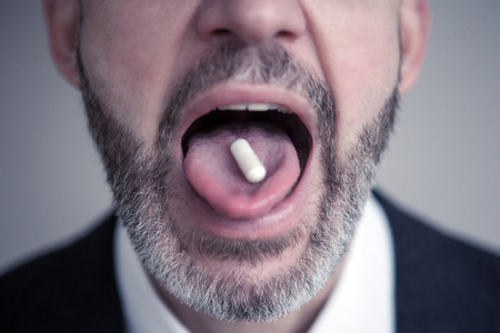 closeup of bearded man with pill on his tongueの写真素材