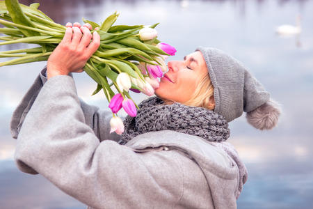 portrait of blond woman in front of lake with tulipsの写真素材
