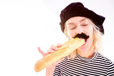 blond woman dressed as a french man with beard and beret eating baguetteの写真素材