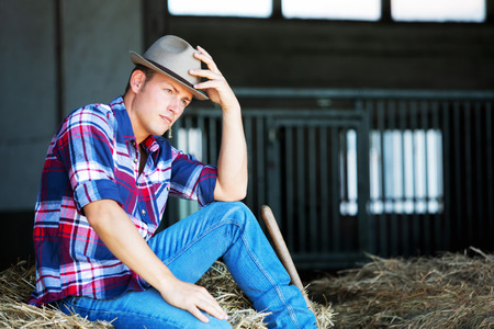portrait of handsome blond man in jeans sitting on haystackの写真素材