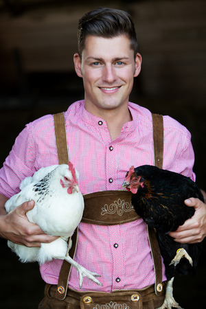 portrait of young bavarian man holding two chickensの写真素材