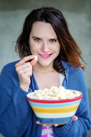 young brunette woman eating popcorn from a bowl and looking at cameraの写真素材