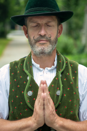 portrait of bavarian man standing outdoors and prayingの写真素材