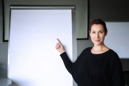 young brunette woman pointing at a flipchart in officeの写真素材