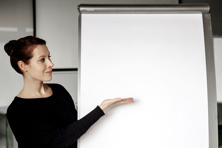 young brunette woman pointing at a flipchart in officeの写真素材