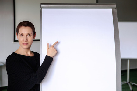 young brunette woman pointing at a flipchart in officeの写真素材