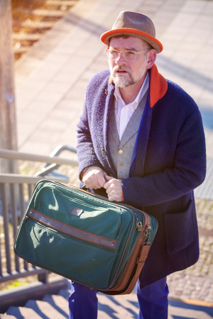 handsome man in his 50s walking with suitcase up stairs at train stationの写真素材