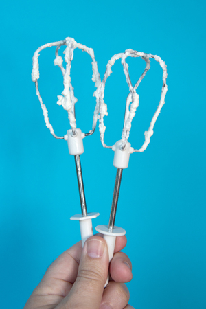 hand holding two beater with whipped cream on blue backgroundの写真素材