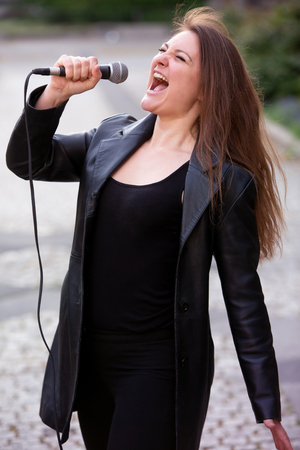 young brunette woman standing and singing with microphone outdoorsの写真素材