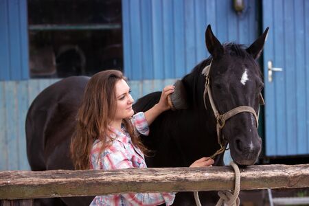 brunette young woman standing outdoors with her black horseの写真素材
