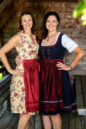 portrait of two bavarian women in dirndl standing by a wooden hutの写真素材
