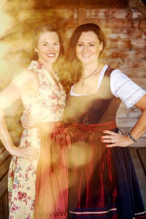 portrait of two bavarian women in dirndl standing by a wooden hutの写真素材