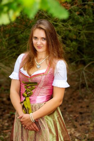 portrait of young woman in dirndl standing by tree and looking lonelyの写真素材