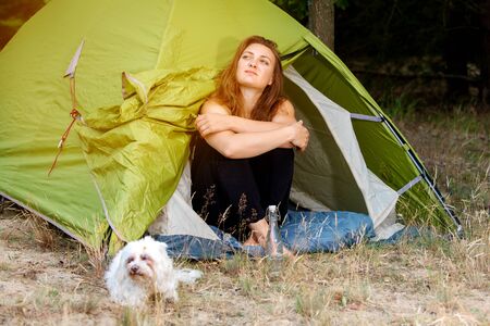 portrait of young woman sitting in front of her tent with her dogの写真素材