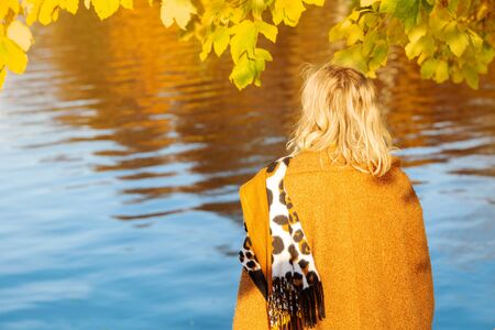 blond woman in her 40s standing by lake and enjoying the autumn sun