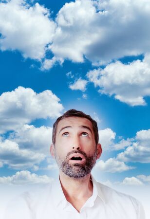 Portrait of a man looking surprised up into the blue skyの写真素材
