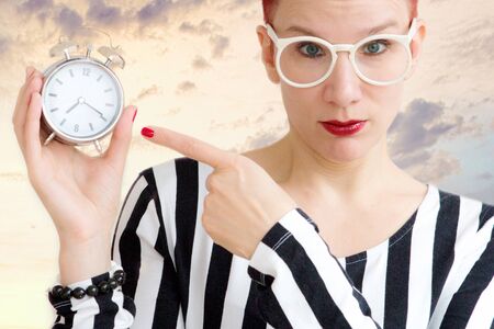 portrait of red-haired woman with glasses holding an alarm clockの写真素材