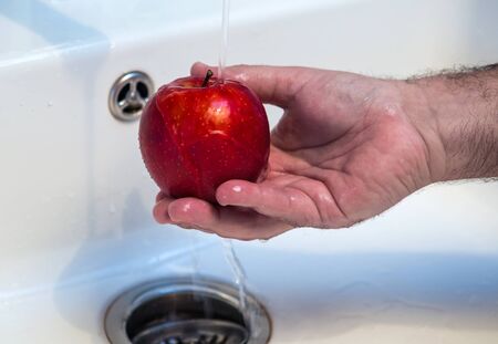 close-up of a mans hand washing a red apple in sinkの写真素材