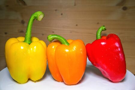 three bellpepers in different colors on plate with wooden backgroundの写真素材