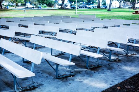 rows of empty white benches in a public parkの写真素材