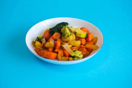 close-up of white plate with mixed vegetables on blue tableの写真素材