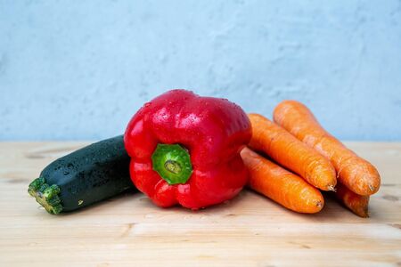 carrots, red bell pepper and courgette on wooden table with grey backgroundの写真素材