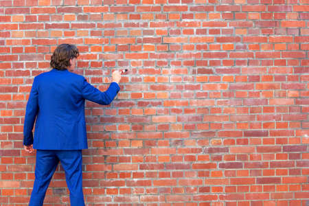 back of businessman in blue suit standing at brick wall with paintbrushの写真素材