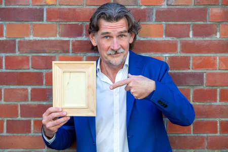 handsome businessman in his 50s in blue suit holding a wooden frameの写真素材