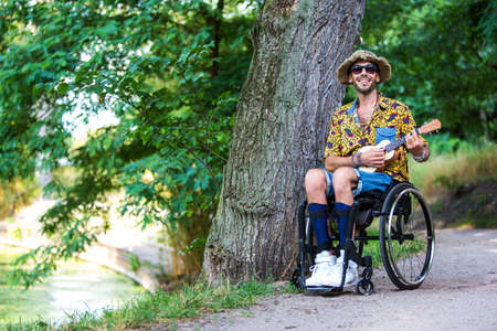handsome man in a wheelchair outdoors in a park playing the guitar
