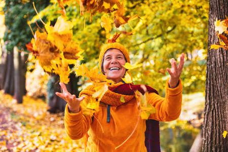happy woman in her 50s outside in autumn playing with falling leavesの写真素材