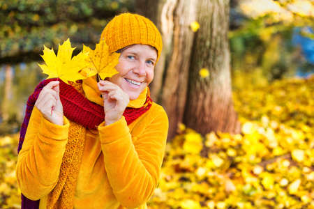 portrait of woman in her 50s standing in park in autumn and playing with leaves