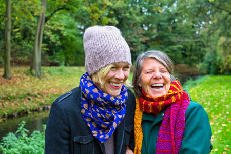 two women in their 50s hugging each other and smiling in a park in autumnの写真素材