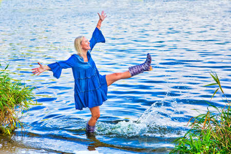 blond woman in a blue dress standing in water with rubber bootsの写真素材