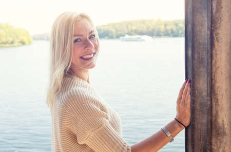 portrait of blond woman by a lake in beige sweaterの写真素材