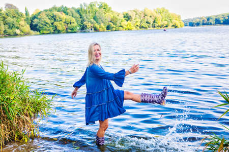 blond woman in a blue dress standing in water with rubber bootsの写真素材