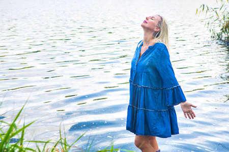 blond woman in a blue dress standing in water with rubber bootsの写真素材