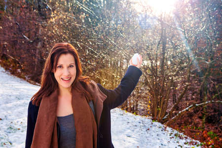 young brunette woman outdoors in the snow holding a snowballの写真素材