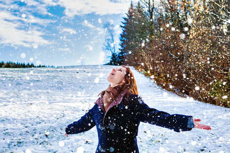 young brunette woman standing in the snow and spreading her armsの写真素材