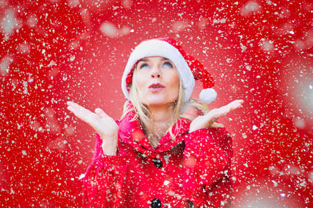 blond woman dressed as Santa Claus on red background and lots of snowの写真素材