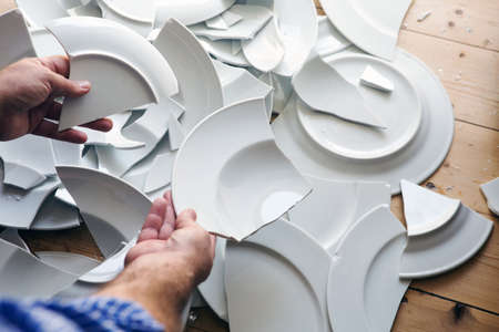 close-up of hands picking up broken white plates on the floor