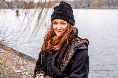 portrait of smiling young woman standing by lake on a snowy dayの写真素材
