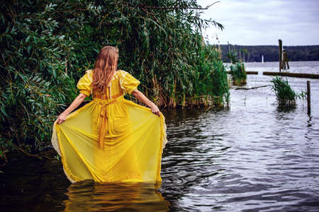 blond woman in yellow historic dress standing in the waterの写真素材