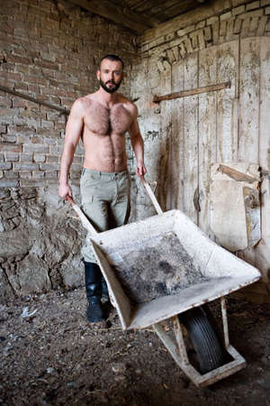 sexy shirtless man standing at a barn with wheelbarrowの写真素材