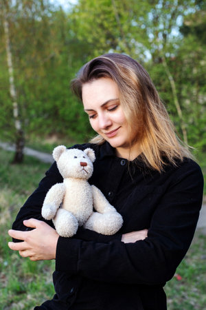 young woman holding a teddy bear outdoors in natureの写真素材