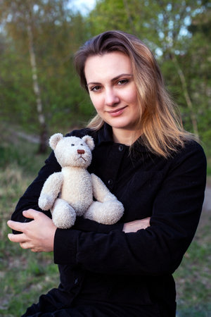 young woman holding a teddy bear outdoors in natureの写真素材