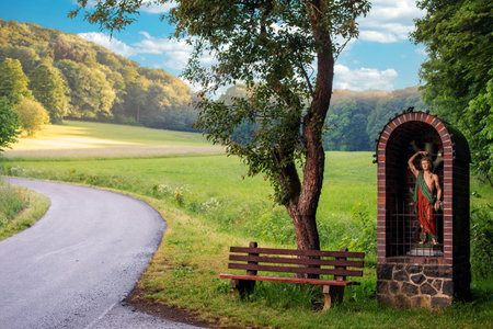 meadow with road and a christian wooden statue with benchの写真素材